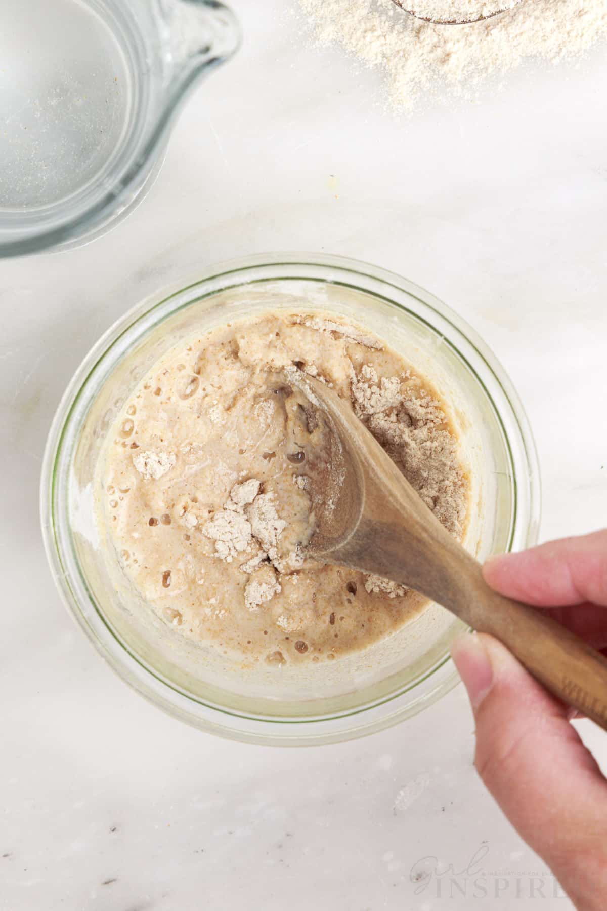 wooden spoon stirring together flour and water in glass jar.