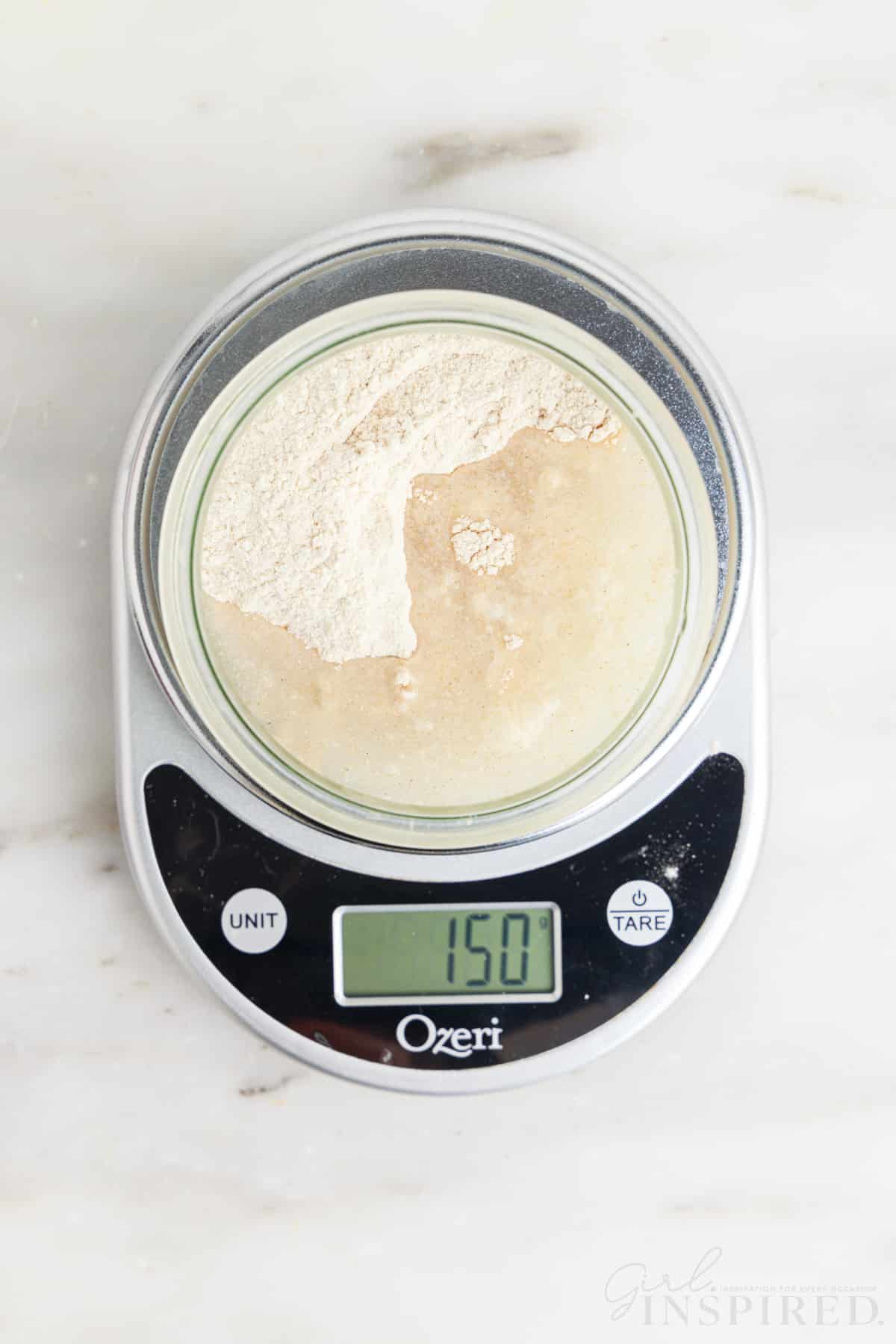 water, flour, and sourdough starter in glass jar on a food scale reading 150 grams.