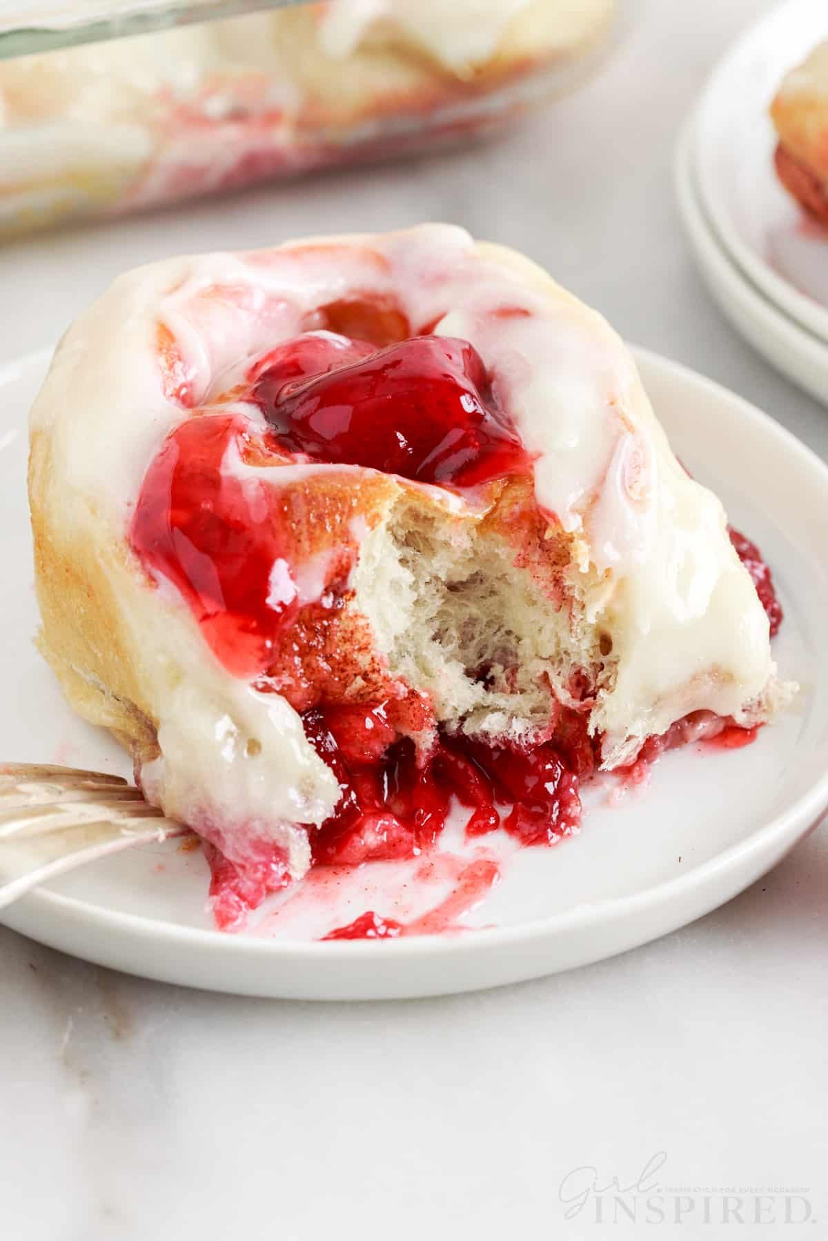 Strawberry cinnamon roll on a plate with a bite taken out.