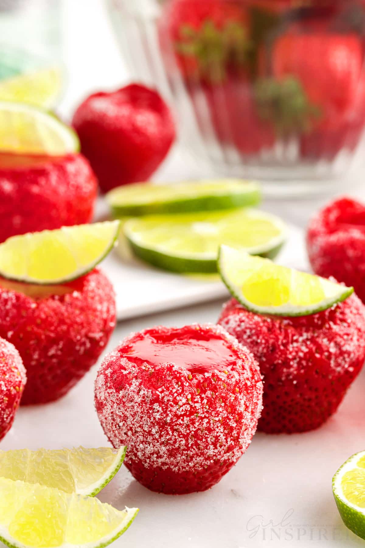 Strawberry daiquiri jello shots set on white counter with sugar coating and lime wedges as garnish.