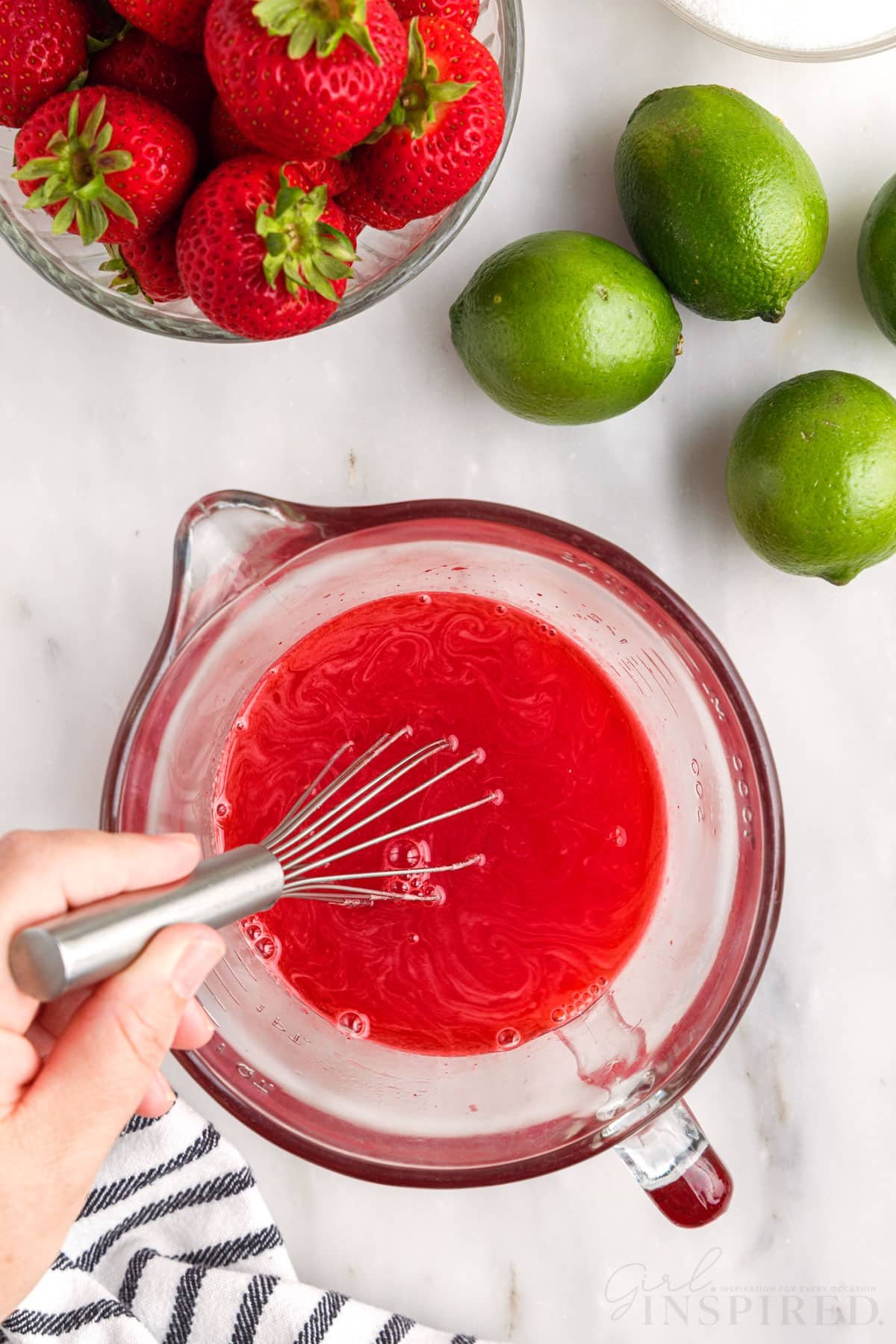 Whisking strawberry gelatin liquid in glass measuring cup.