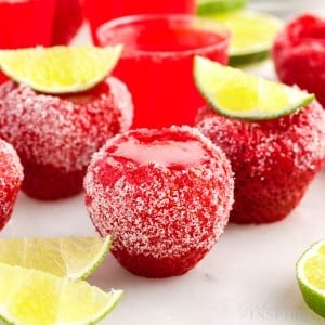 Strawberry daquiri jello shots set on white counter with sugar coating and lime wedges as garnish.