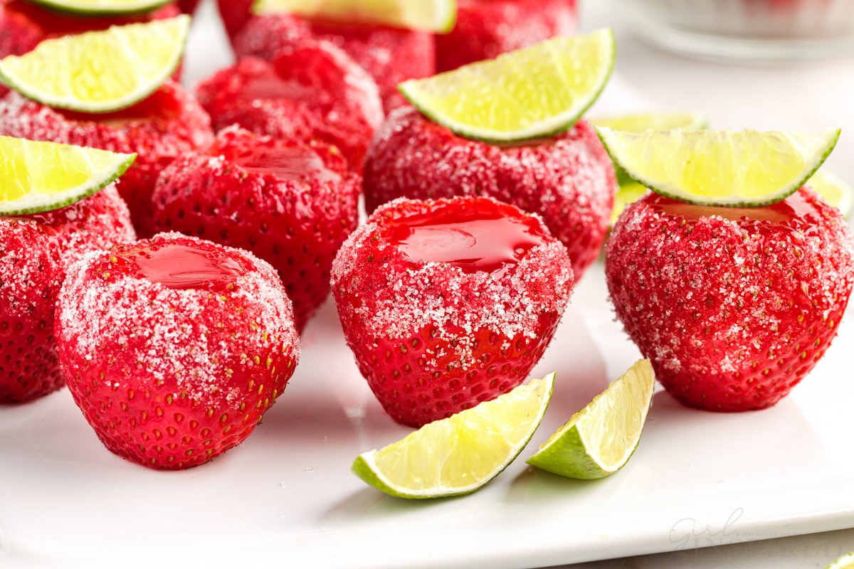 Strawberry daquiri jello shots set on white counter with sugar coating and lime wedges as garnish.