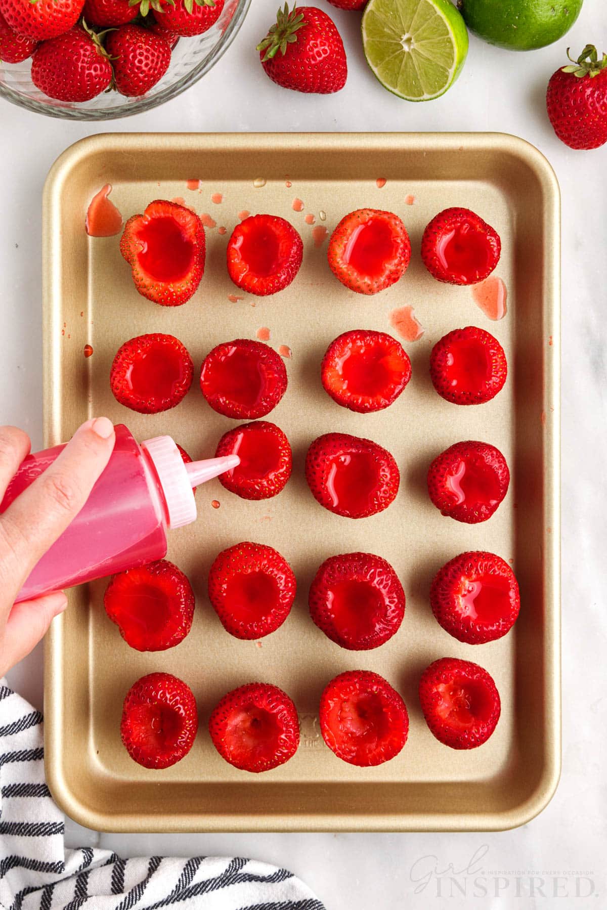 Squeeze bottle squirting jello into hollowed out strawberries on sheet pan.