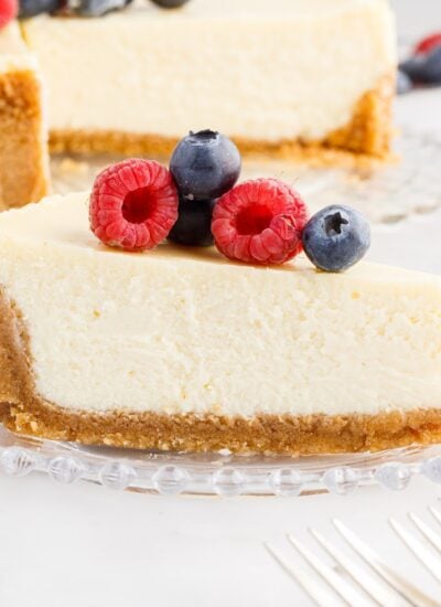 Slice of Classic Cheesecake with graham cracker crust with berries on top.