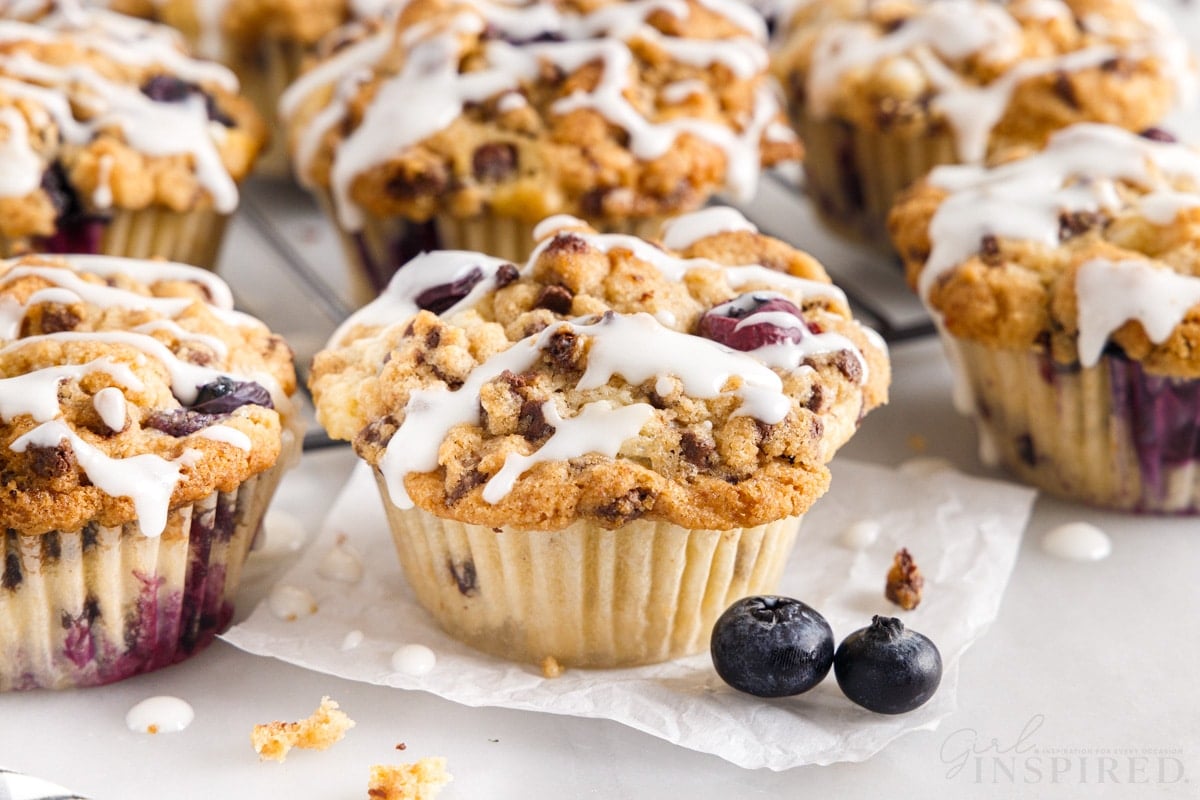 Blueberry chocolate chip muffins on a tray with sugar glaze drizzled over the top.