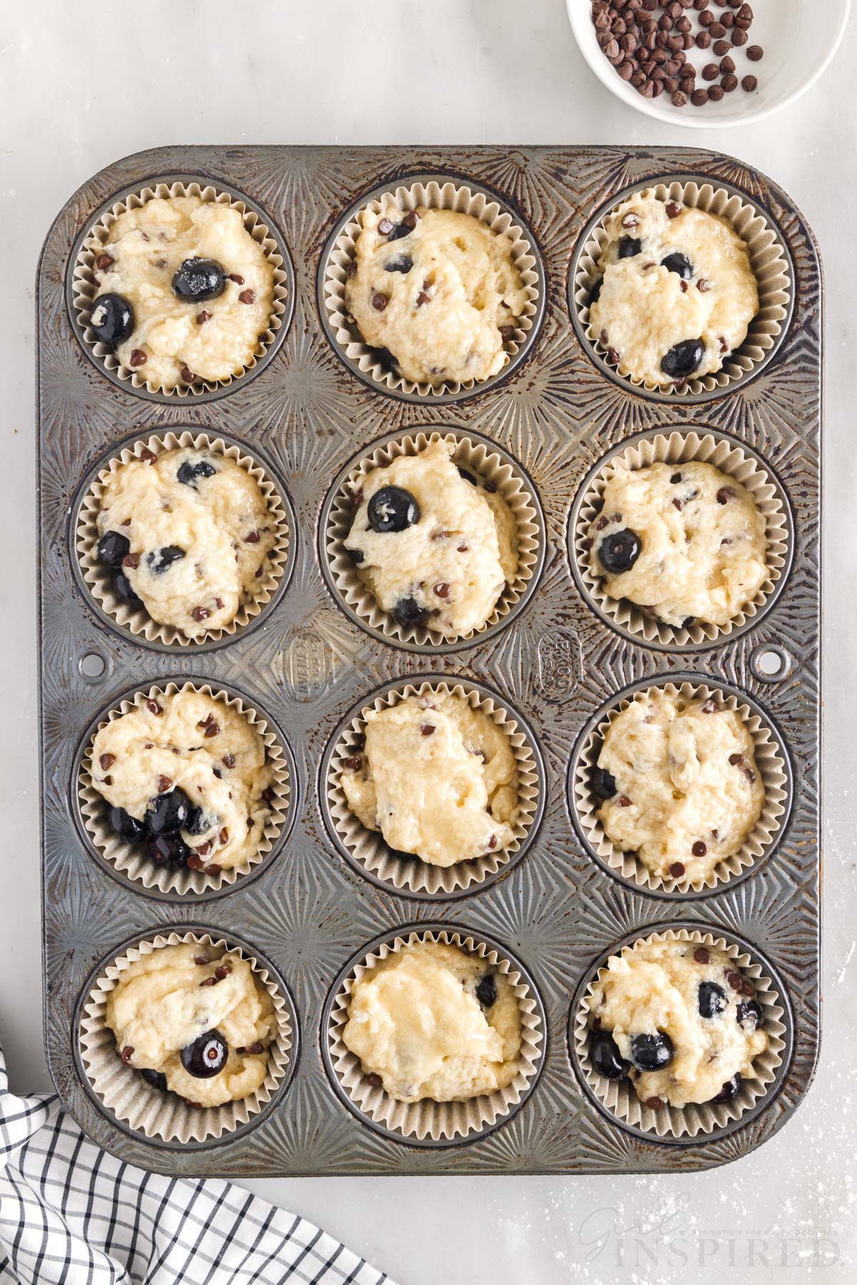 12-cup muffin tin with blueberry chocolate chip muffin batter filling each cup.