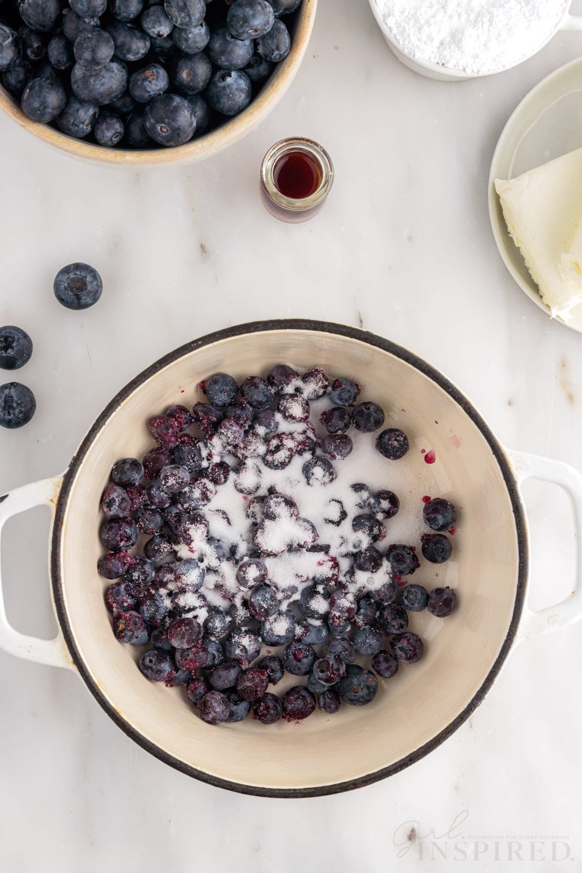 Blueberries and sugar in dutch oven next to blueberries.