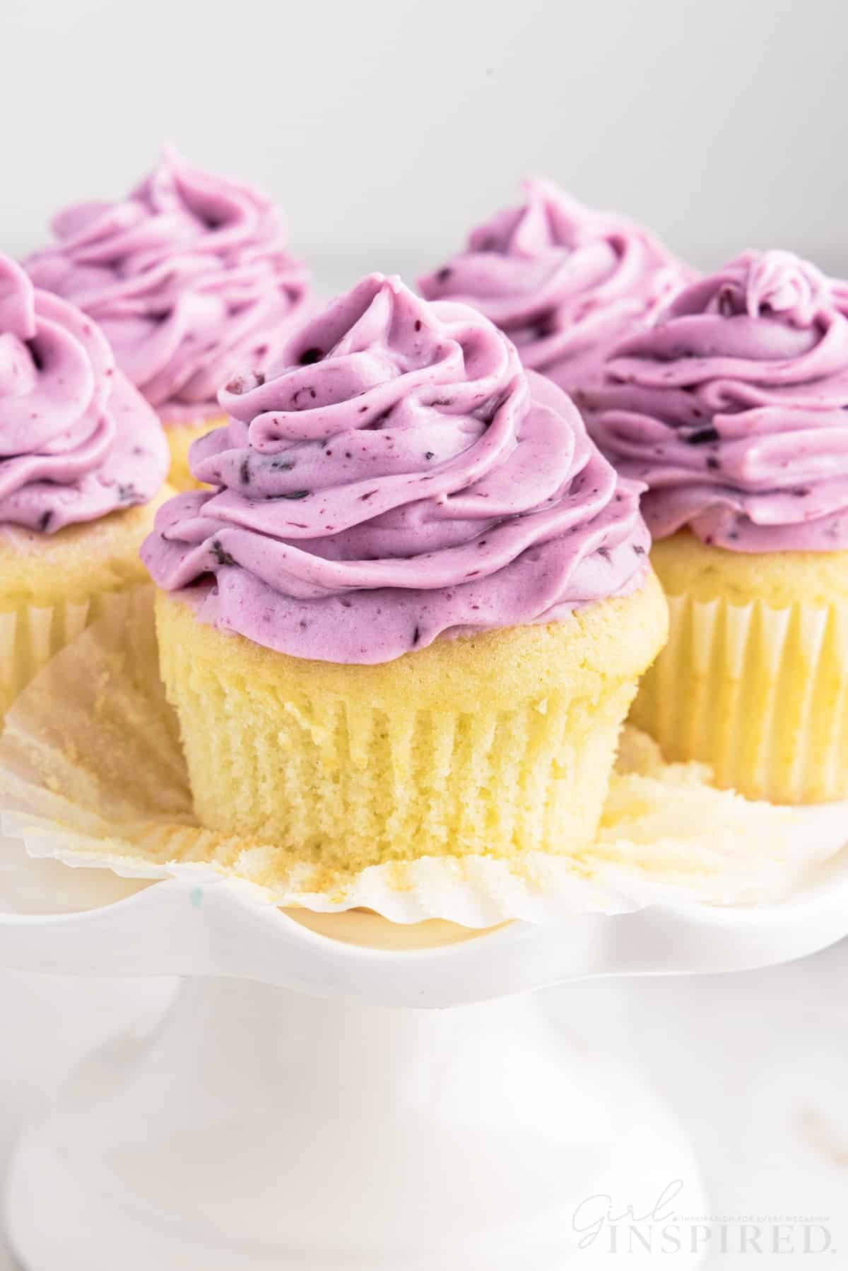 Blueberry Cream Cheese Frosting on cupcakes on a cake stand.
