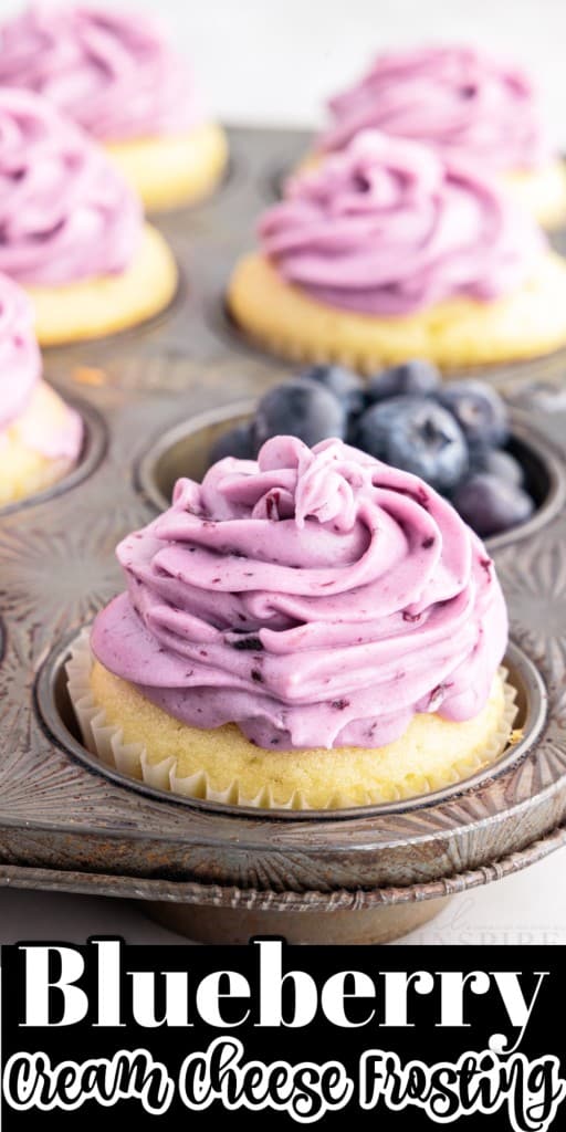 A muffin tin with Blueberry Cream Cheese Frosting covered cupcakes, one slot filled with blueberries.