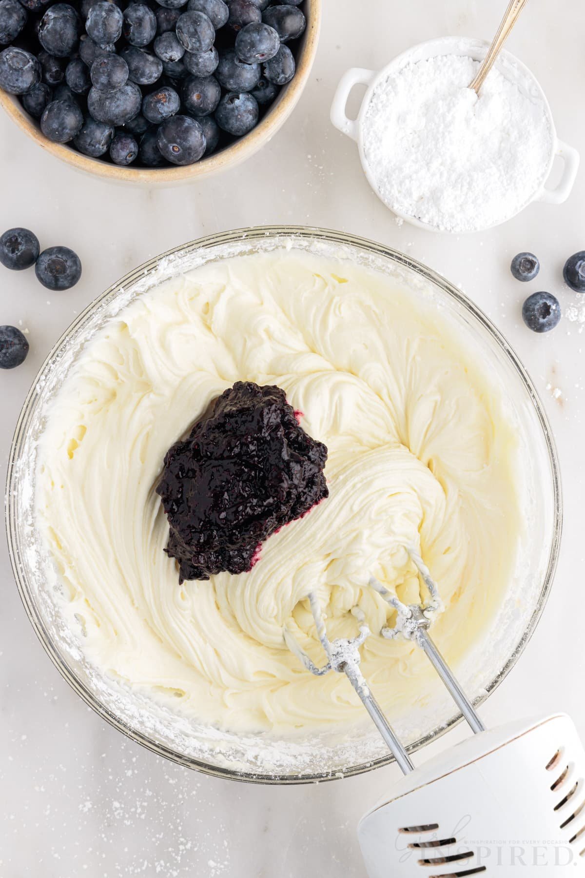 Blueberry reduction added to butter mixture hand mixer inserted.