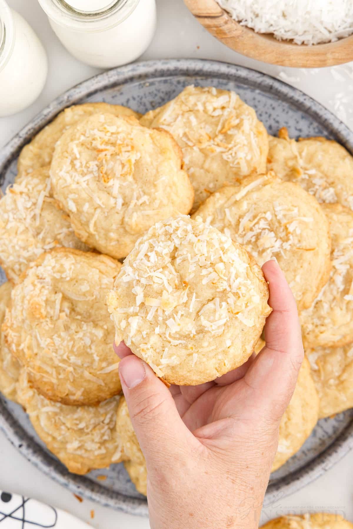 Chewy Coconut Cookies on a plate on being held above the plate.