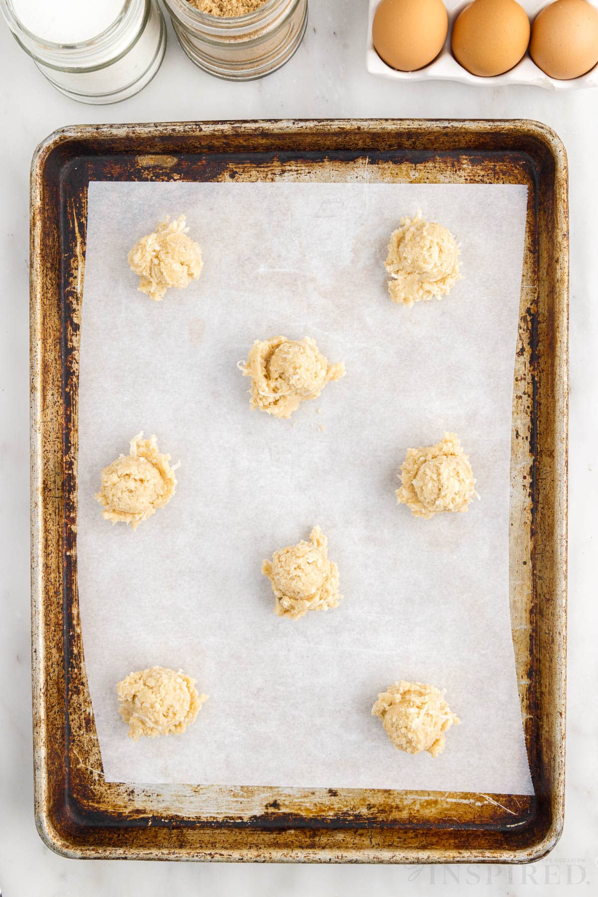 Eight balls of Chewy Coconut Cookies on a parchment lined cookie sheet.