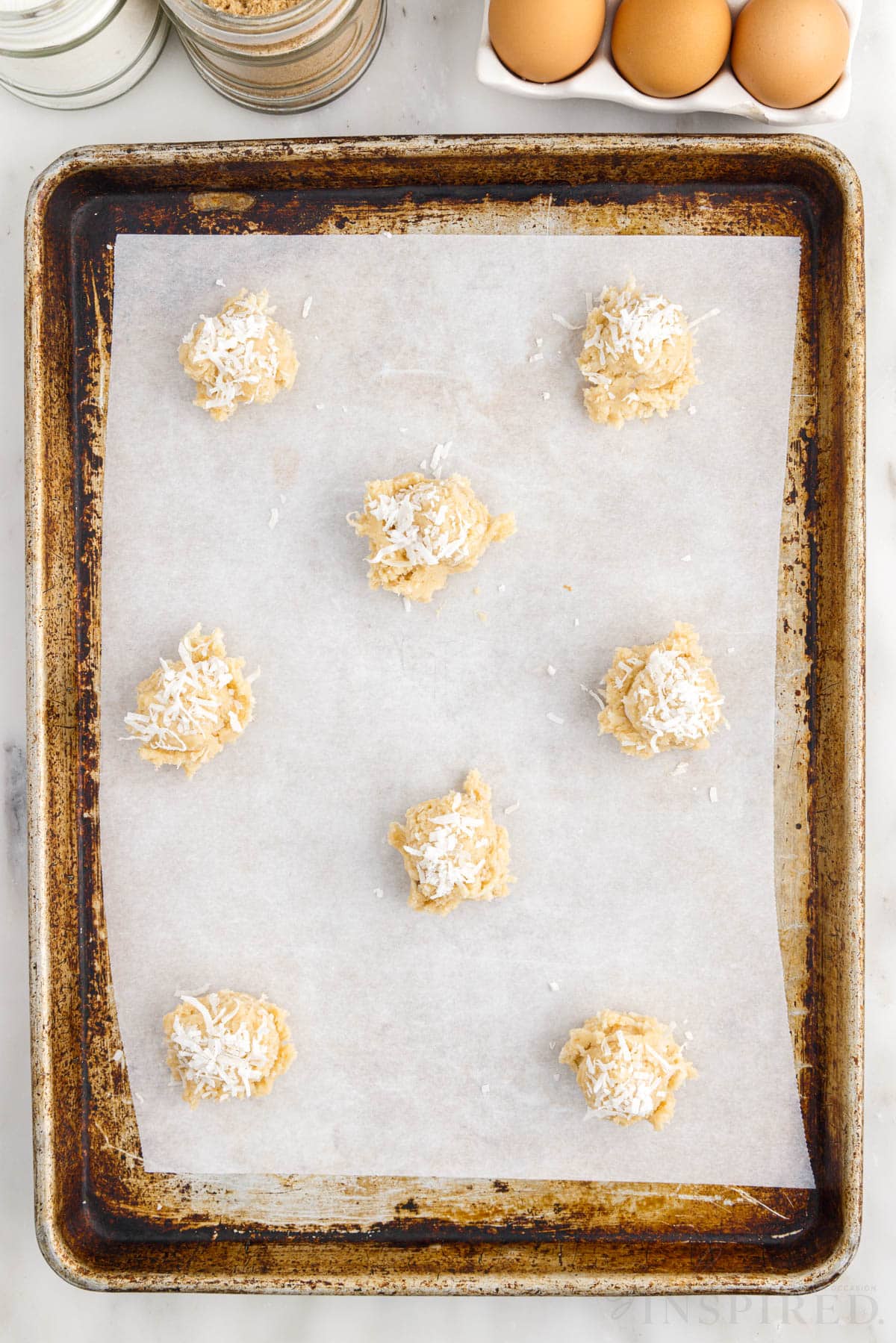 Coconut added to the top of the balls of dough on a cookie sheet.