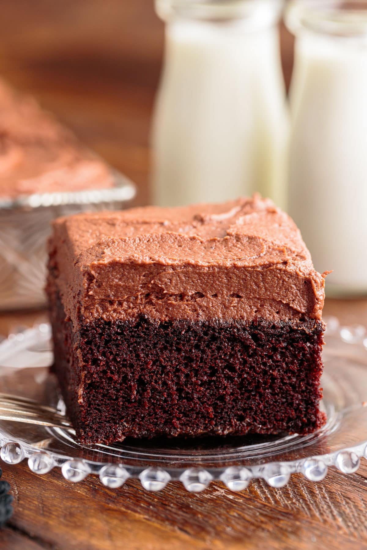 Front view of a slice of Chocolate Mayonnaise Cake on a plate with milk in the background.