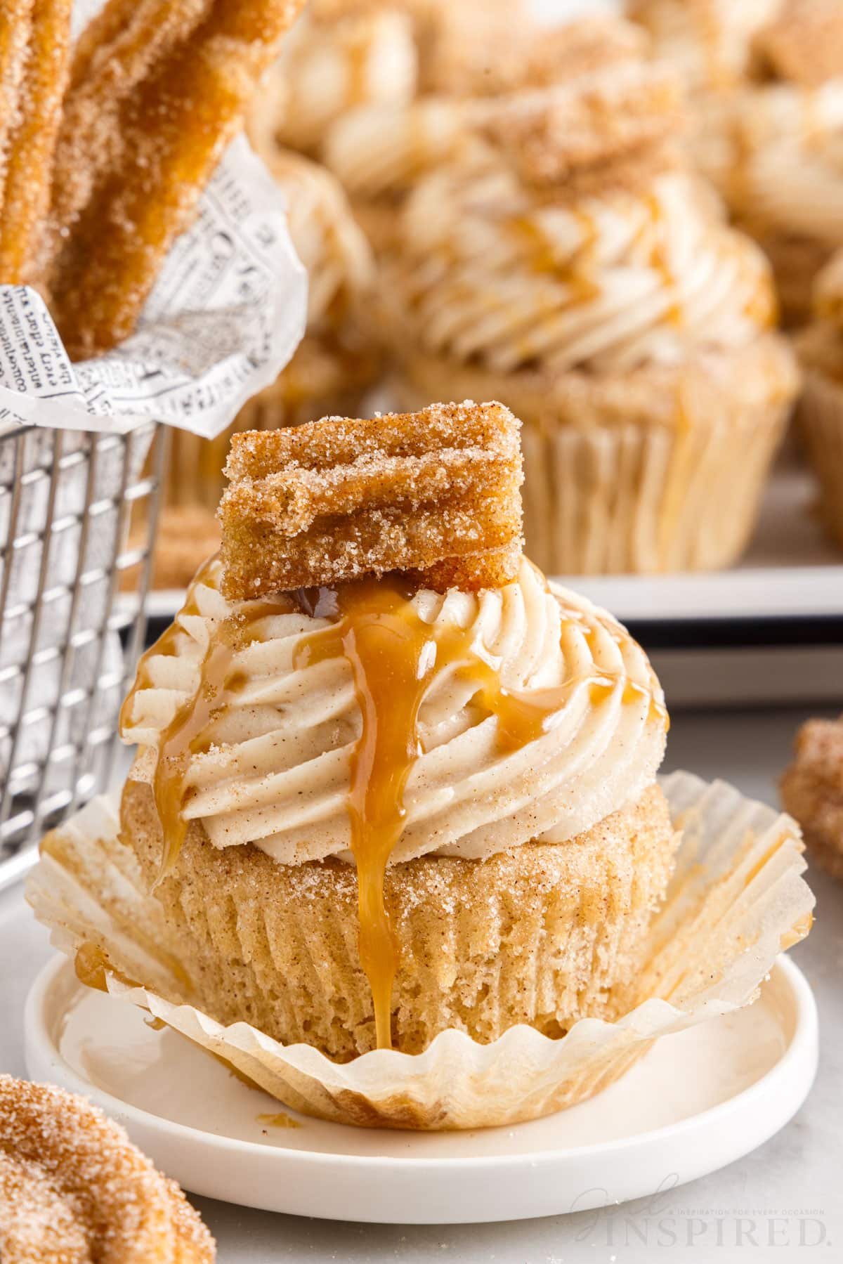 Paper peeled down from a Churro Cupcake on a dish, Churros and additional Churro Cupcakes in the background.