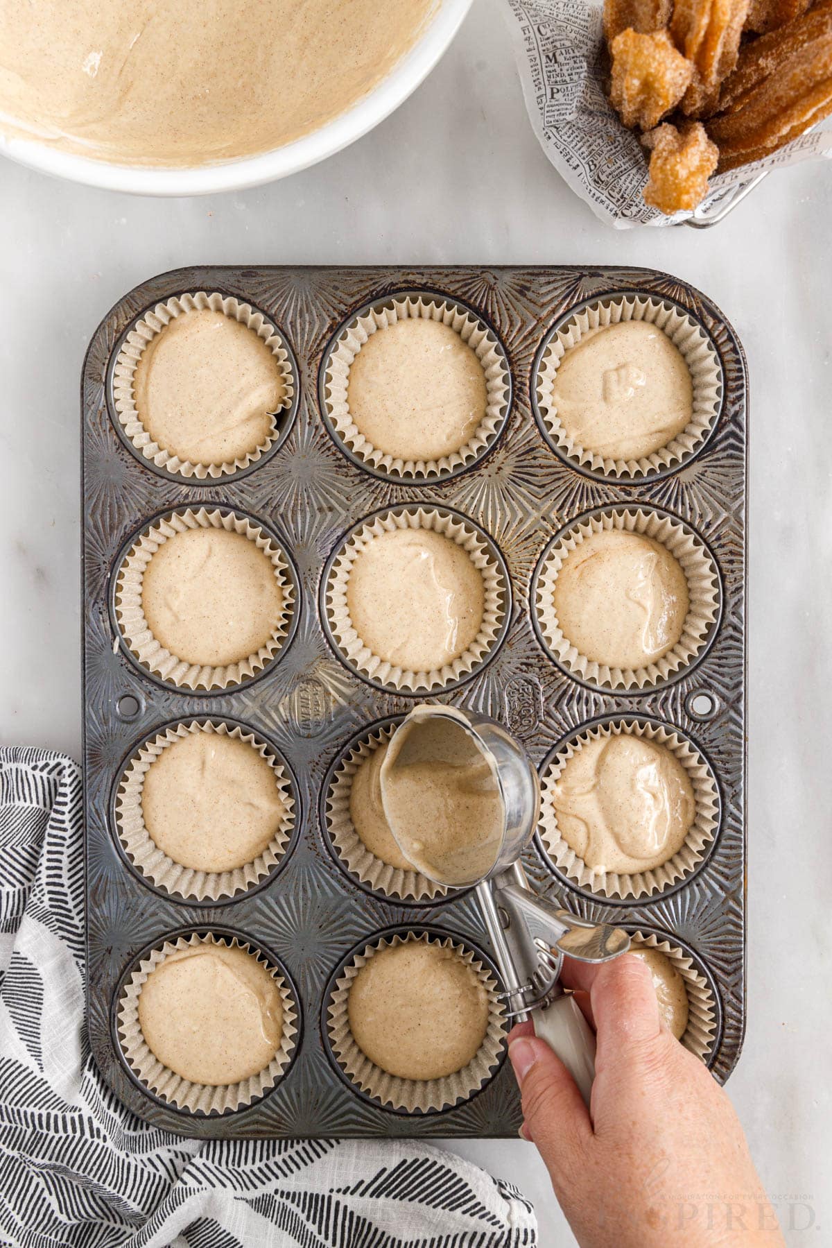 A lined muffin pan with Churro Cupcake batter being added to it.