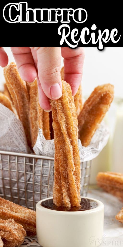 A Churro being dipped in a small dish of chocolate, a wire basket in the background of Churros.