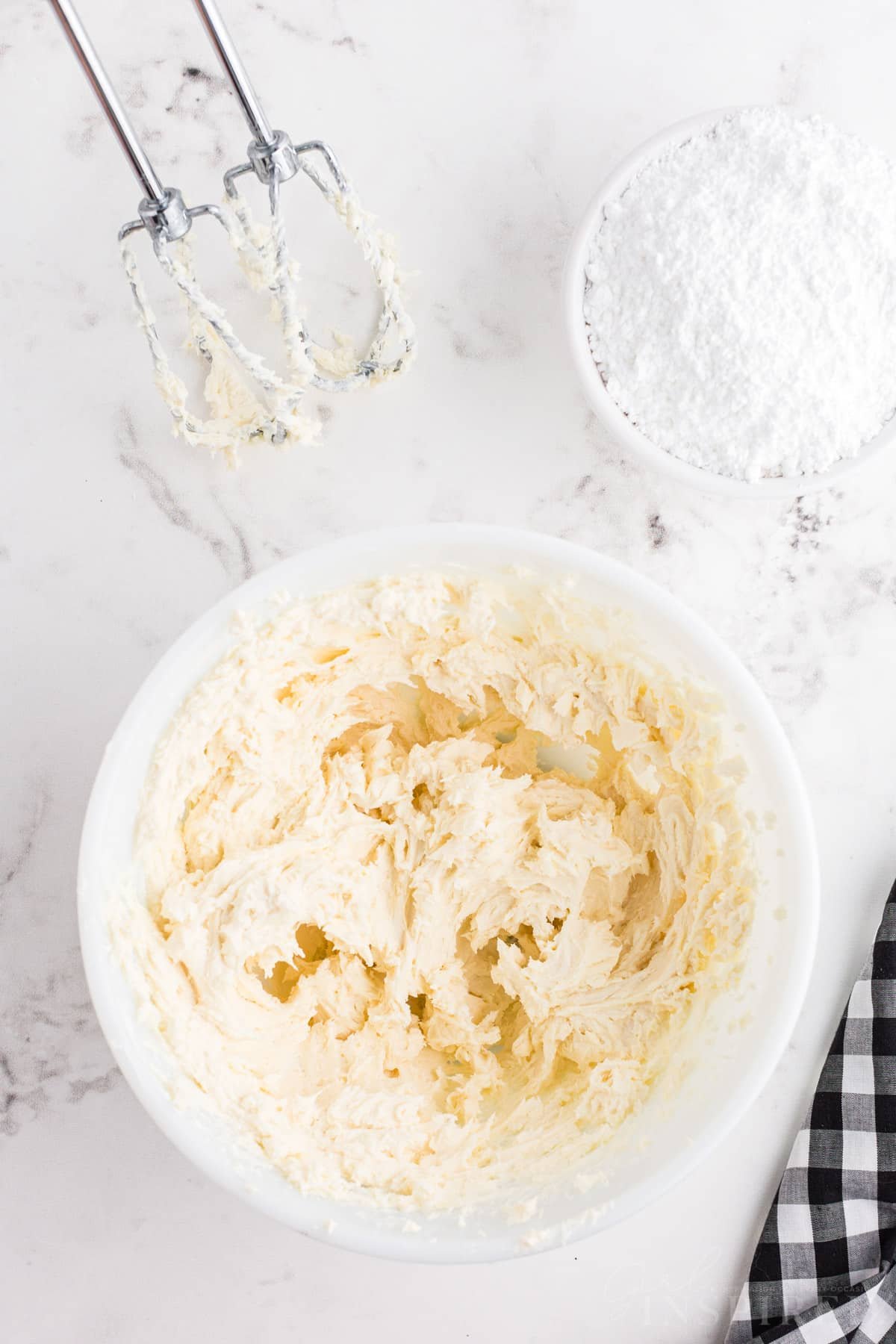 Bowl with mixed butter, cream cheese, and vanilla extract, hand mixer attachment with mixture.