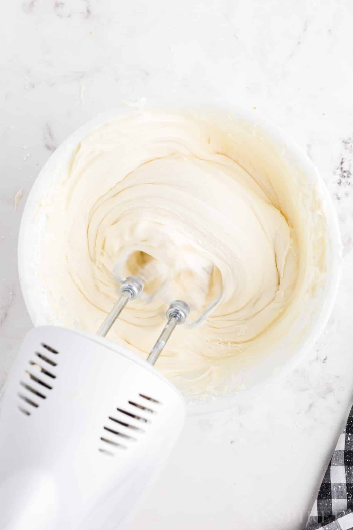 Electric mixer beating the cream cheese buttercream ingredients in a mixing bowl.