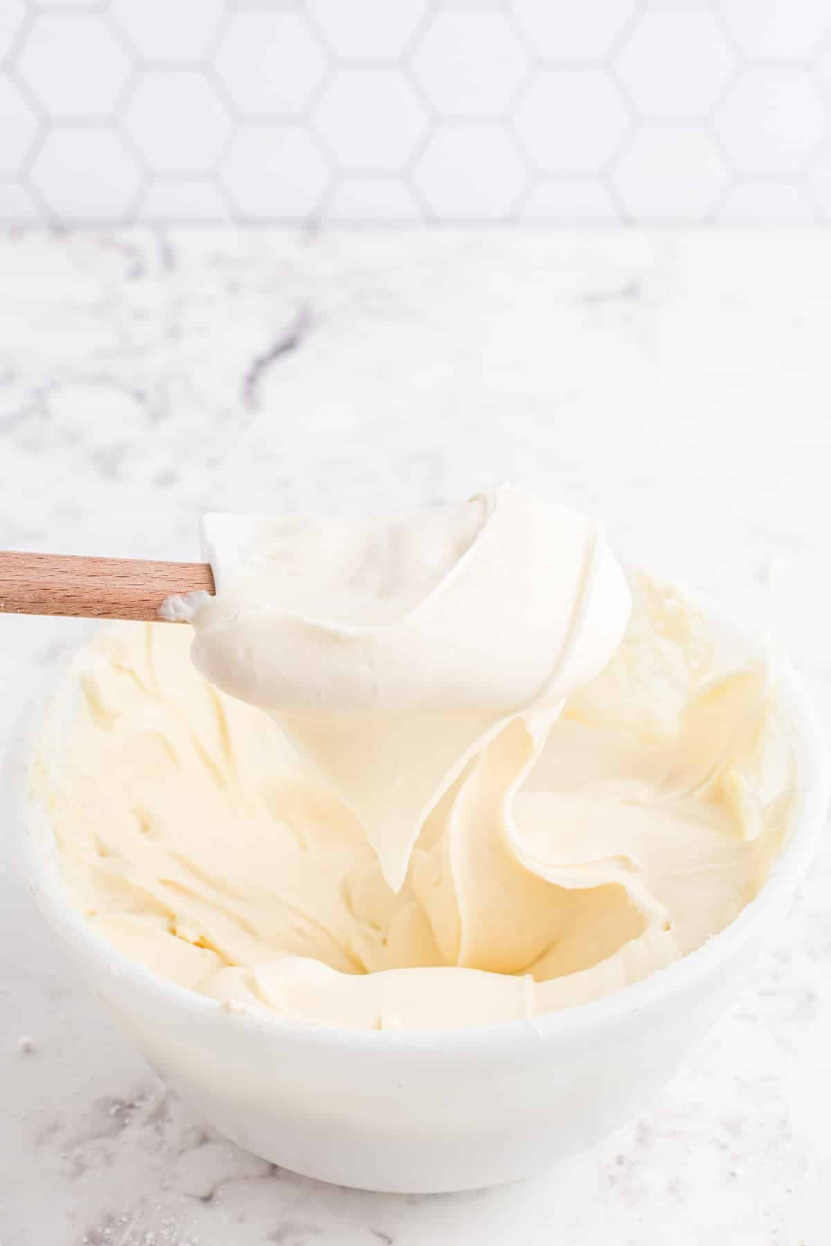 Plastic spatula held above a mixing bowl with cream cheese buttercream frosting.