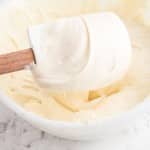 Close up of plastic spatula and mixing bowl with cream cheese buttercream frosting.