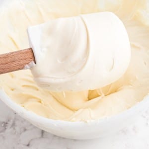 Close up of plastic spatula and mixing bowl with cream cheese buttercream frosting.