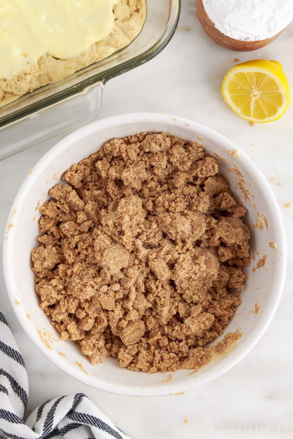 Bowl of streusel topping, baking dish with lemon coffee cake layers.