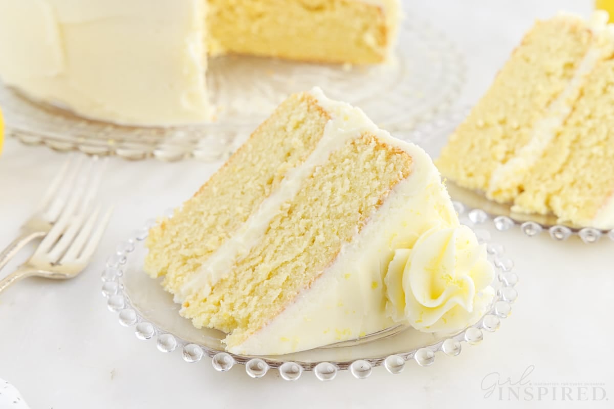A close up of two slices of Lemon Layer Cake next to two forks, the cake in the background.