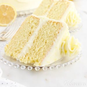 Two slices of Lemon Layer Cake on plates next to forks and a half of a lemon.