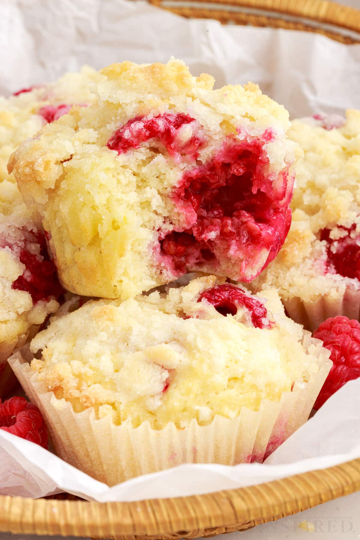 Lemon Raspberry Muffins in a basket lined with paper and a bite taken from the top one.