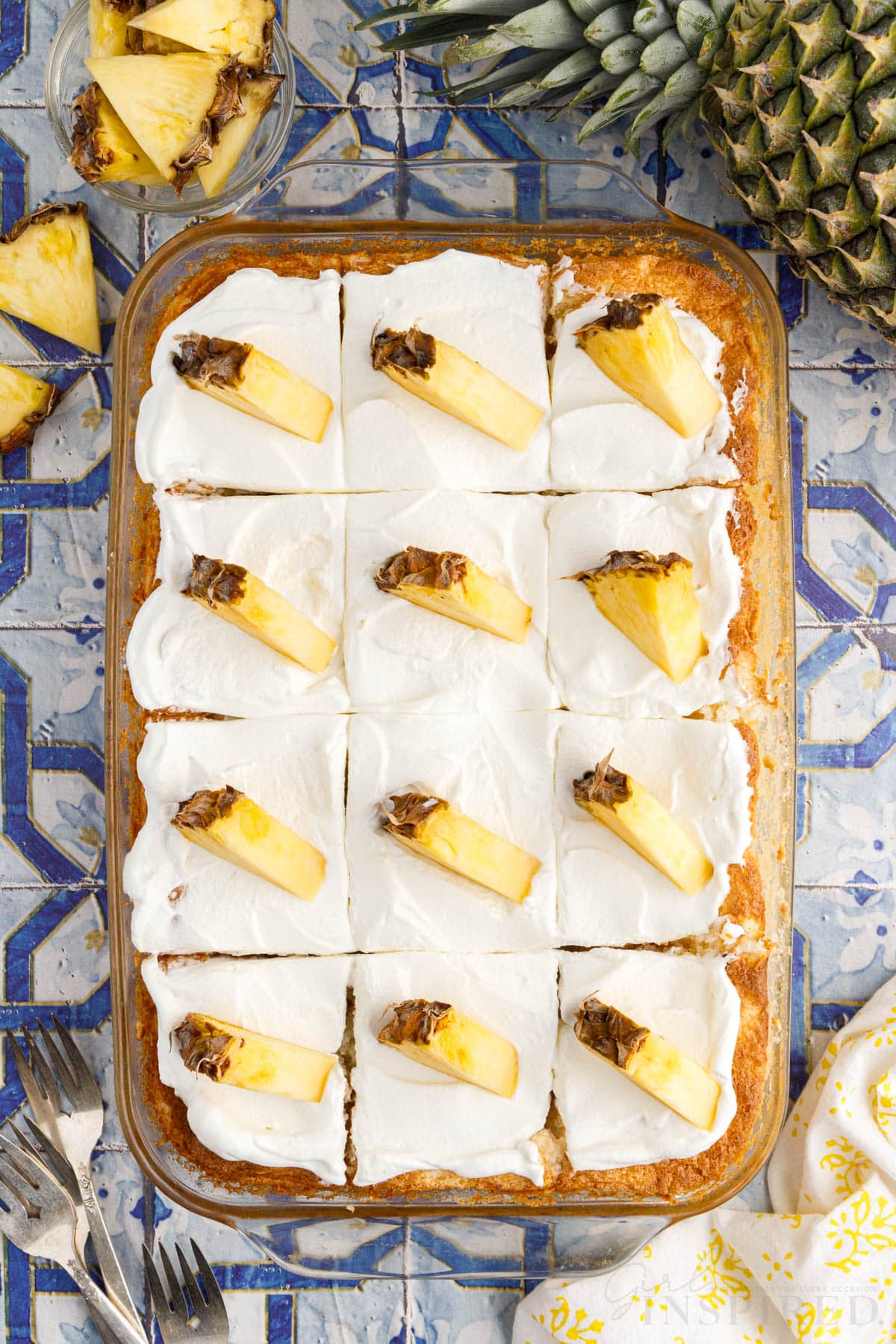 Overhead view of pineapple angel food cake in glass casserole dish, sliced into 12 squares and garnished with a pineapple wedge on top of each slice.