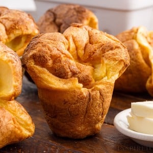 Close up of popovers on a cutting board next to butter.