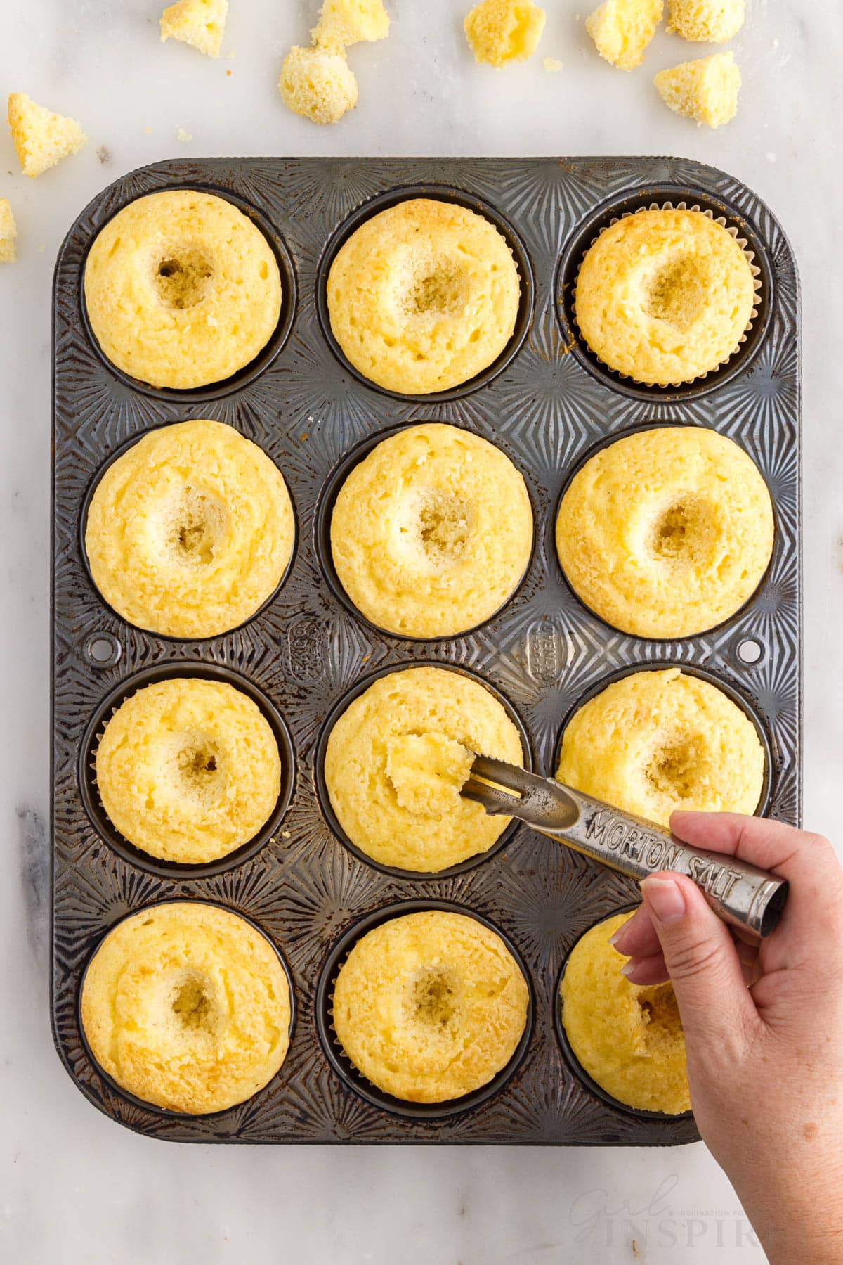 Serrated spoon carving out a small hole in each cupcake in muffin tin.