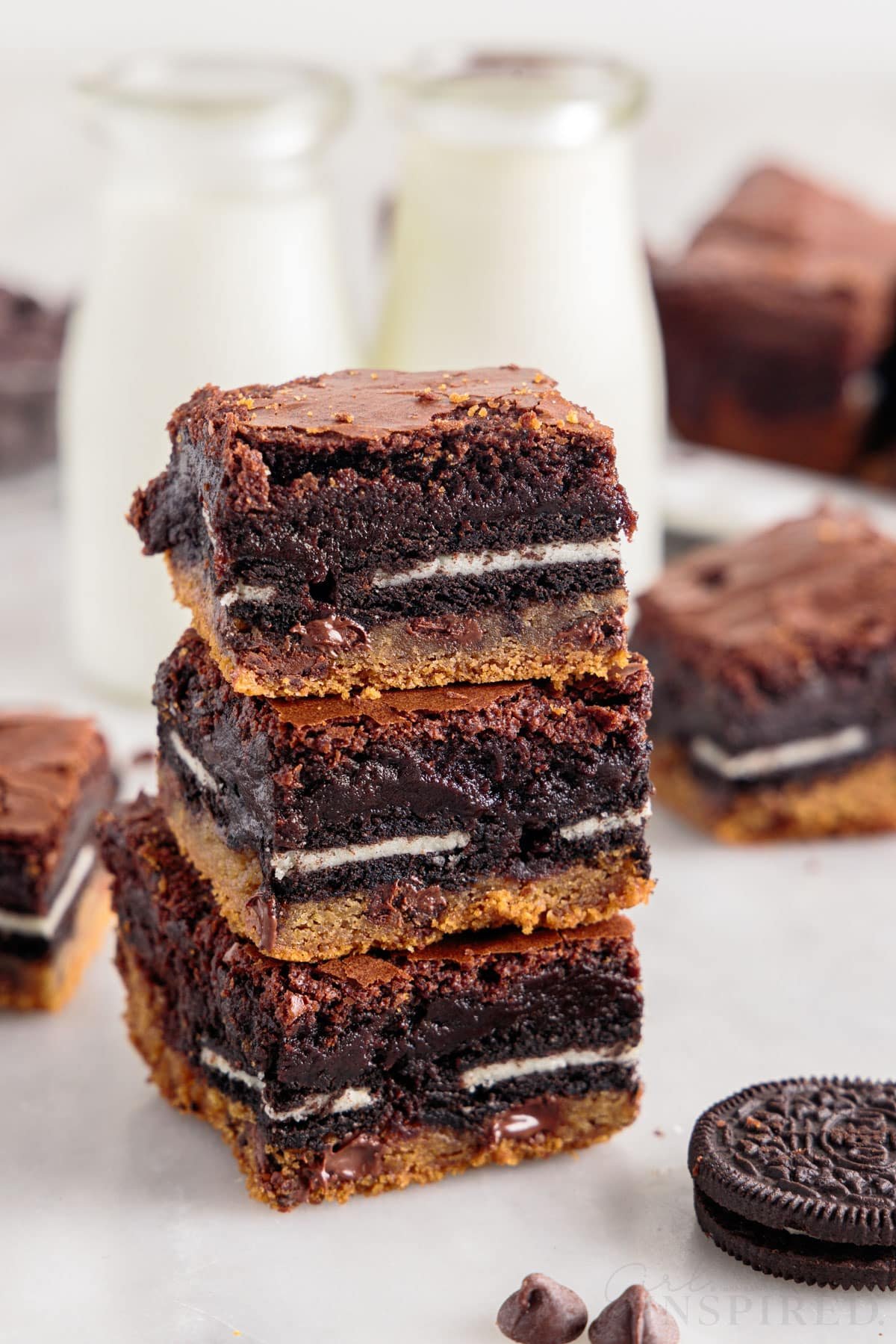 Three Slutty Brownies stacked on each other with brownies and milk in the background.