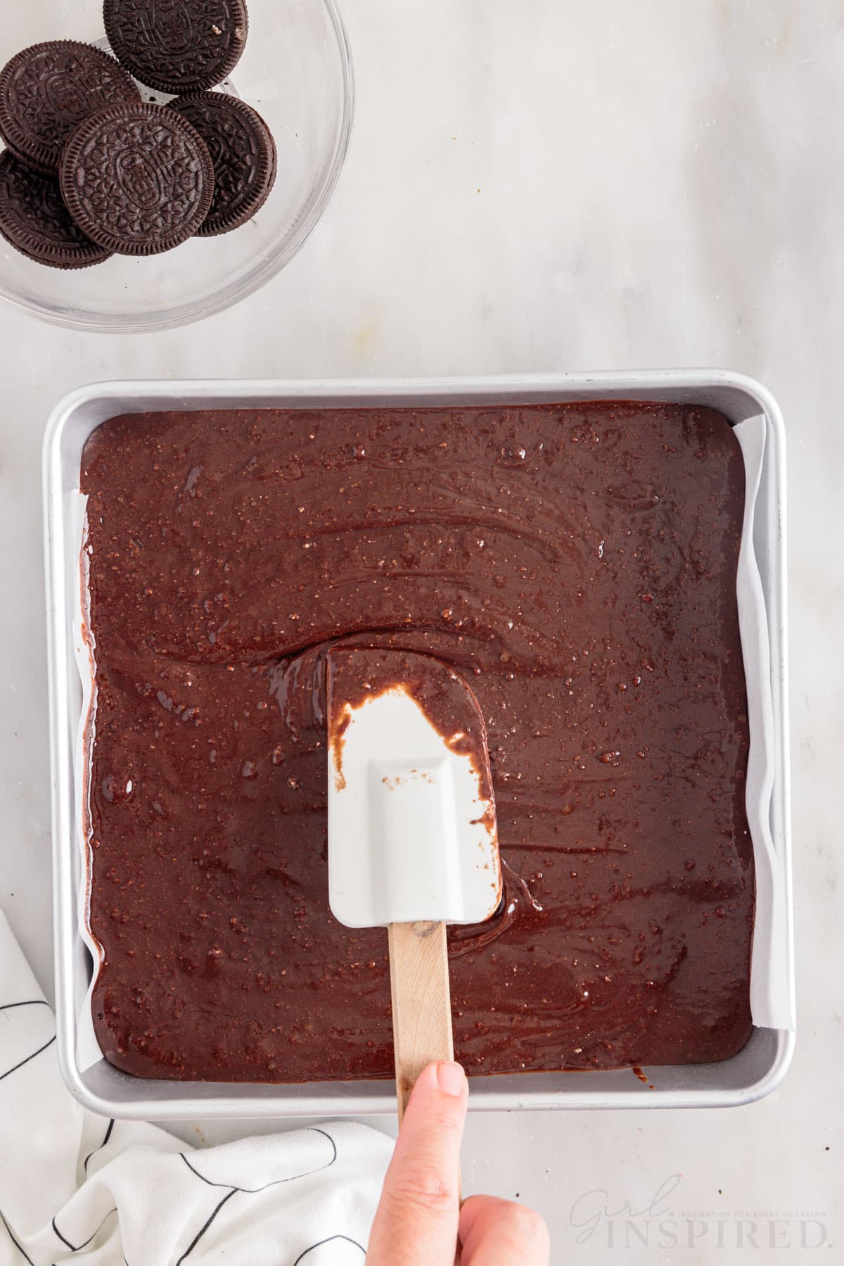 Brownie batter being smoothed with a spatula next to a bowl of Oreo's.