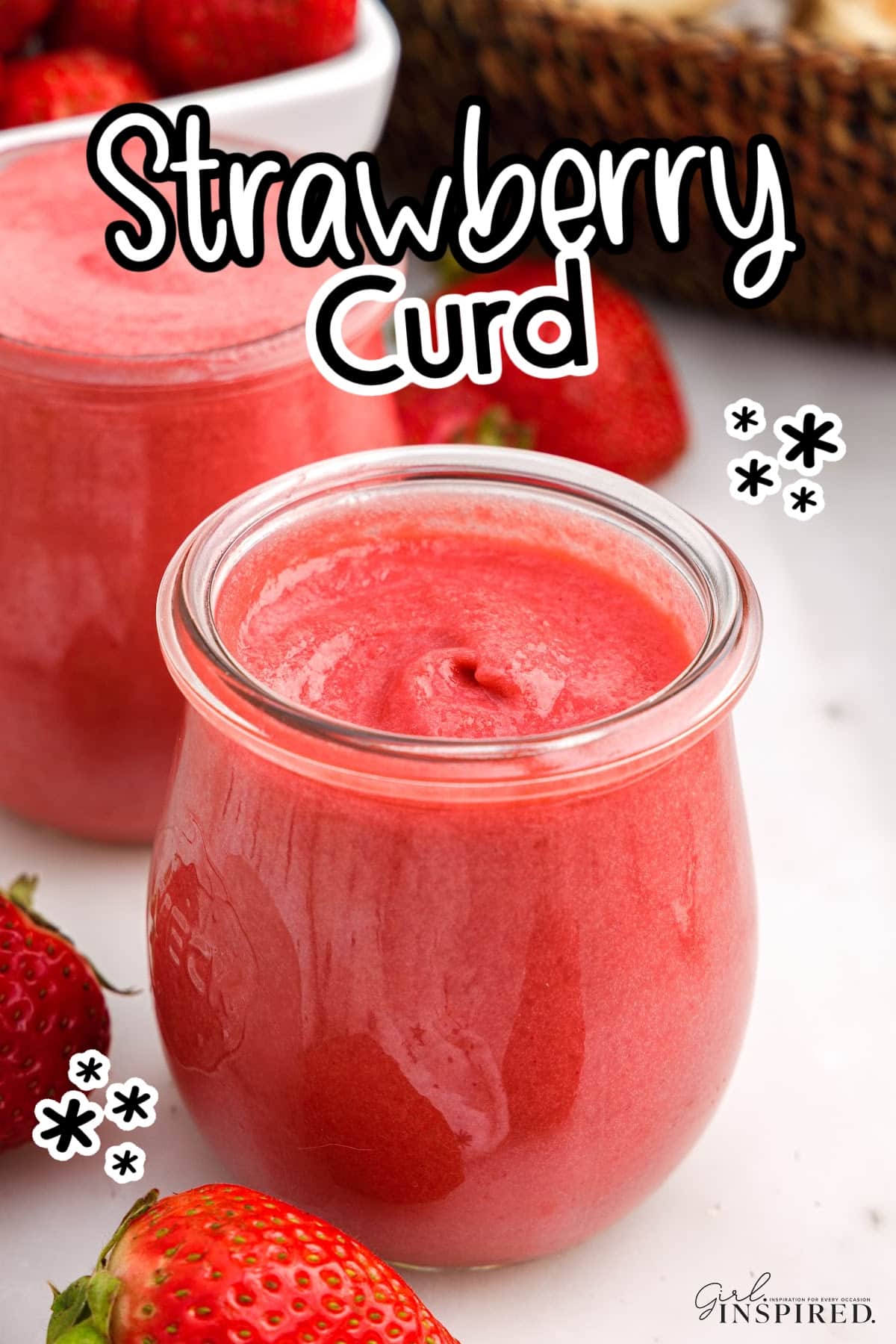 Small glass jar of strawberry curd with fresh strawberries and additional jars in background.