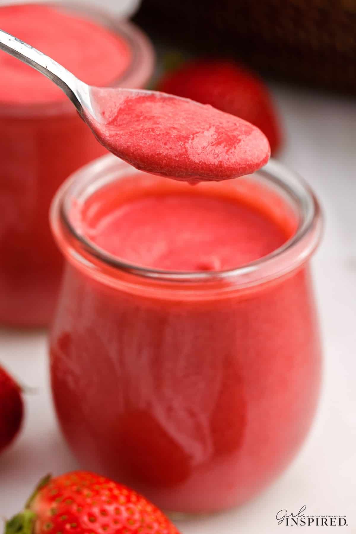Spoonful of strawberry curd held over small jar of the curd.