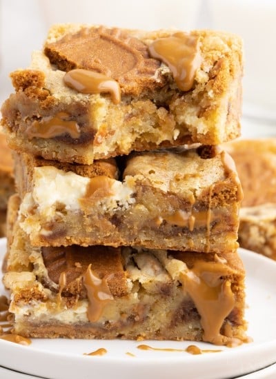 Two small round plates stacked on each other with three Biscoff Blondies stacked on top of each other with a bite taken from the top.