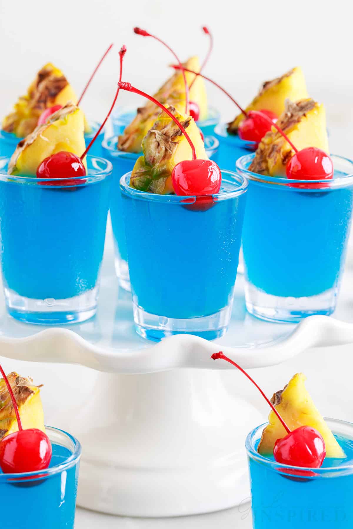 Blue Hawaiian Jello Shots on a cake tray and two in front.