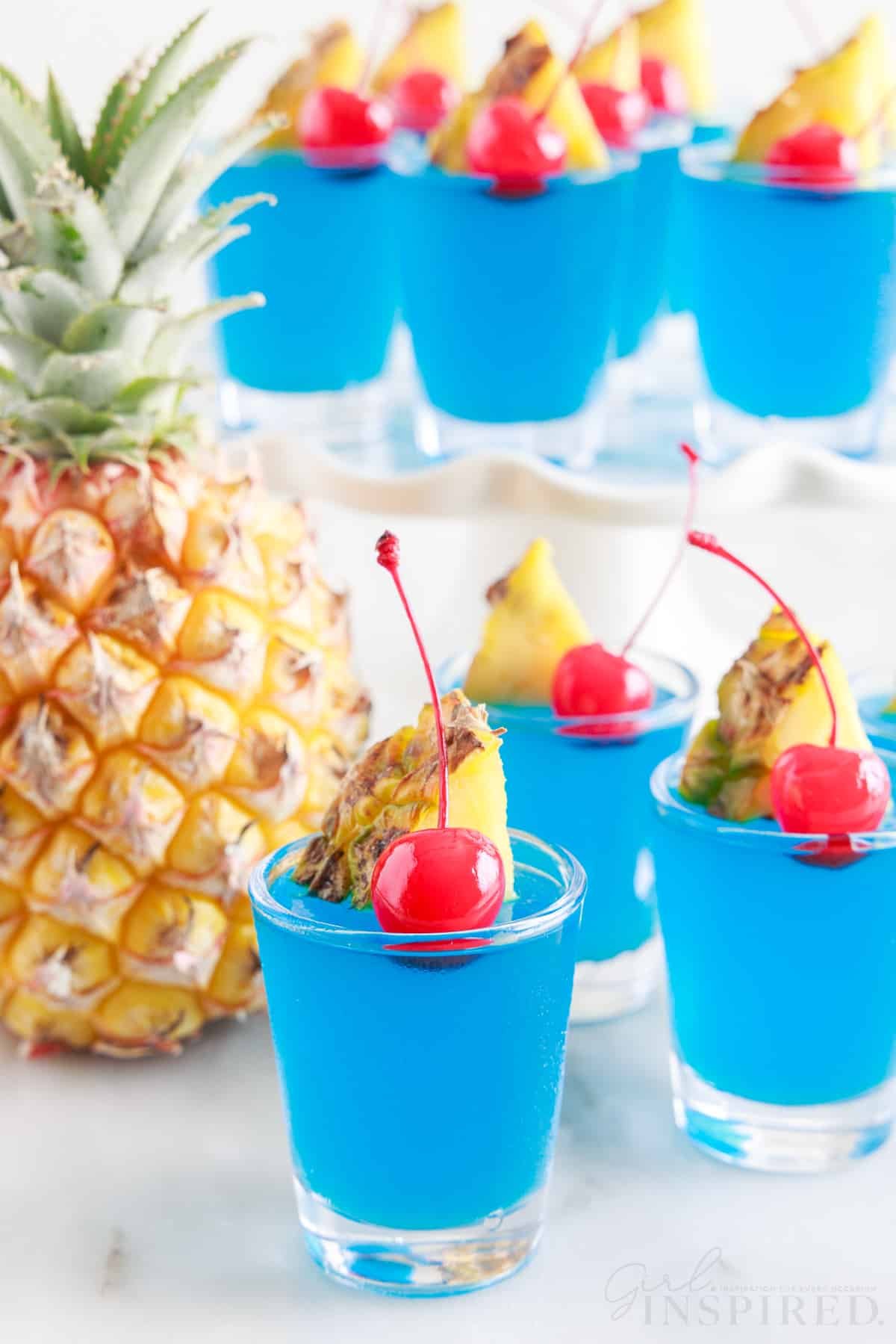 Blue Hawaiian Jello Shots on the counter and a tiered tray with a pineapple.
