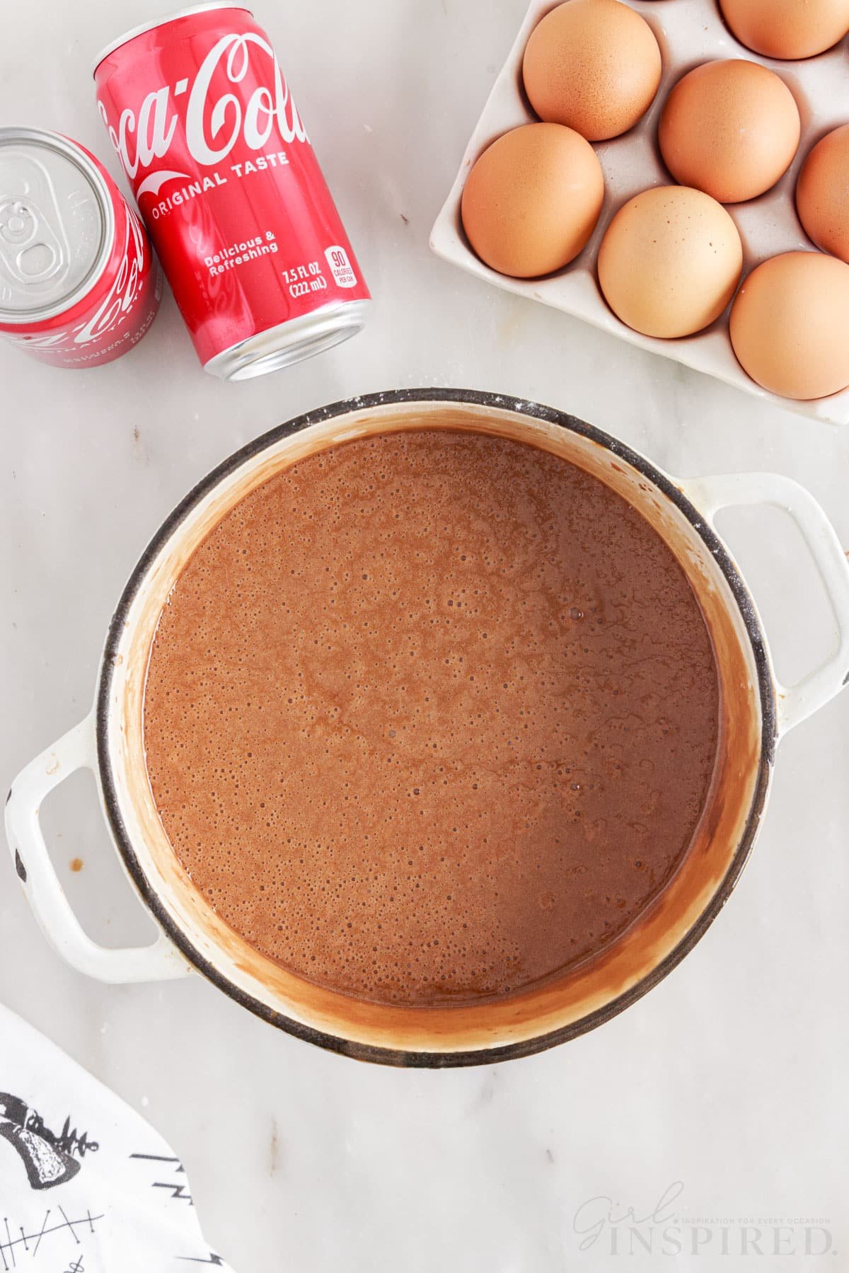 Coca Cola Cake batter in pan next to eggs and two Cokes.