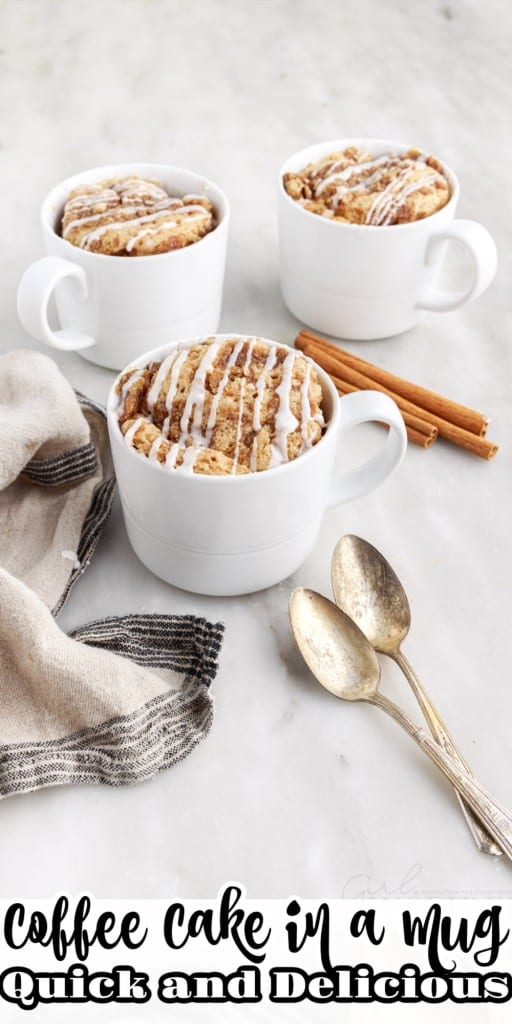 Front view of three coffee cakes in mugs along with some cinnamon sticks, spoons and a linen cloth on the side on a white countertop