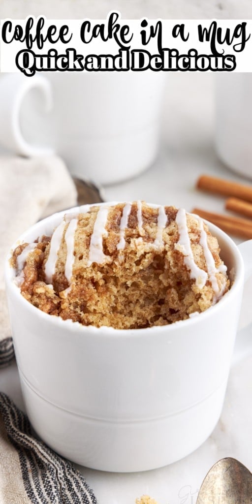 A bite taken from Coffee Cake in a Mug with more coffee cake mugs in the background along with cinnamon sticks and a linen cloth on the side