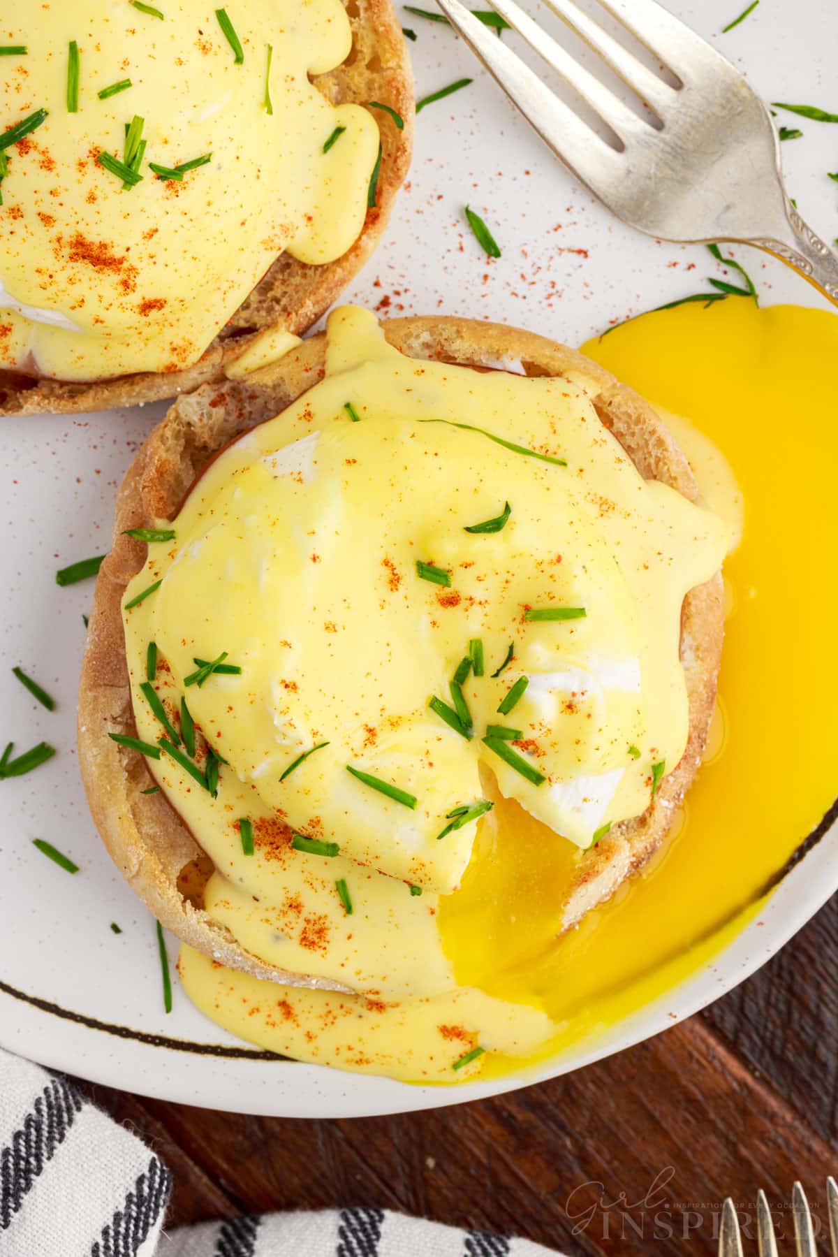 Overhead view of Classic Eggs Benedict with hollandaise sauce on top next to a fork.