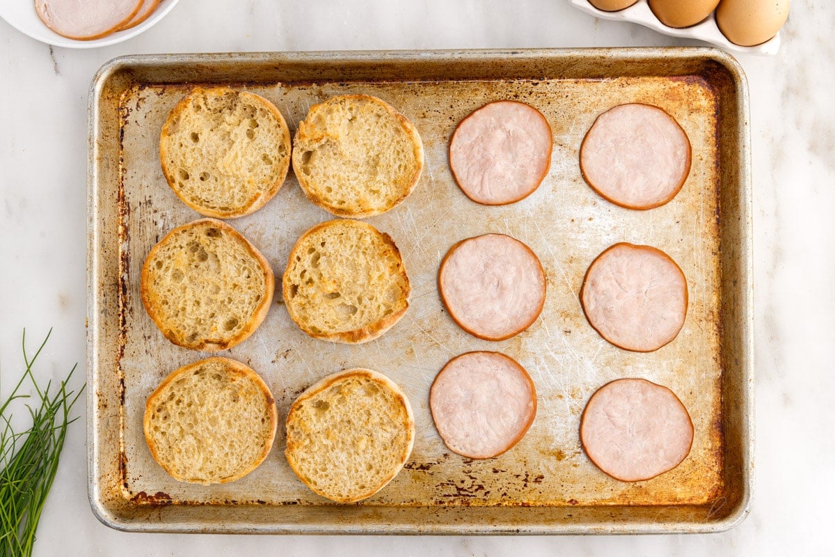 Canadian bacon and English muffins after being baked on a cookie sheet.