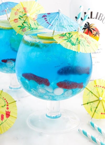 Close up of two goblets of Fish Bowl Drinks with yellow and blue drink umbrellas and Malibu in the background.