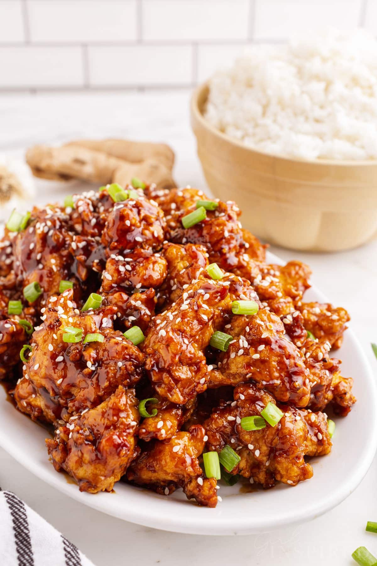 General Tso Chicken on a white serving plate, bowl of white rice in the background.