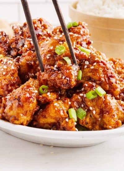 Chopsticks inserted in a dish full of General Tso Chicken on white kitchen countertop.