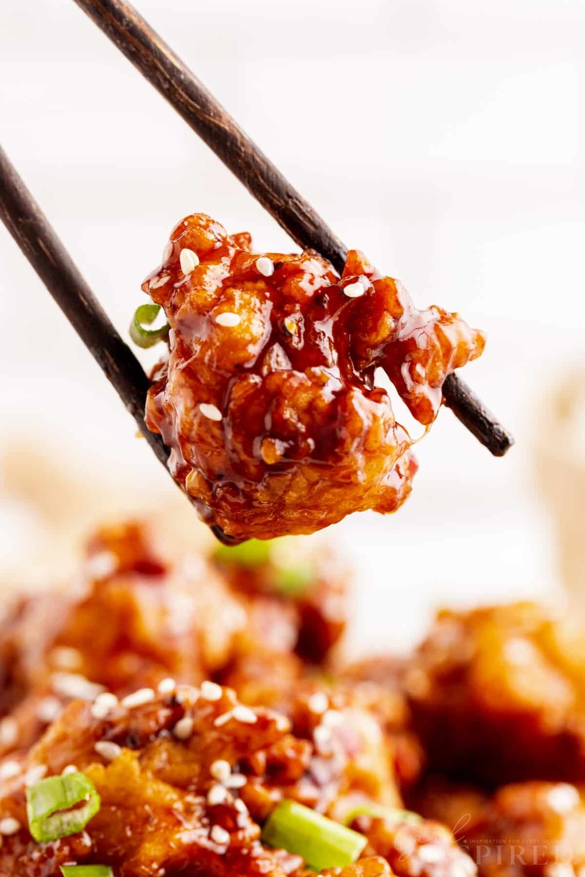 Chopsticks holding a piece of General Tso Chicken.